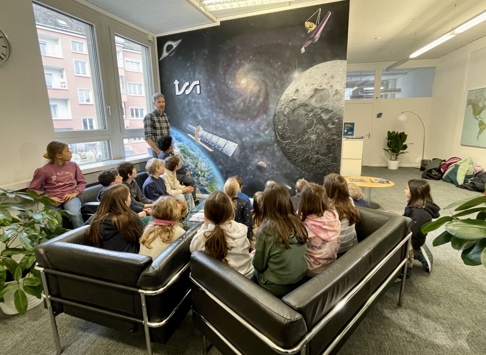 A school class visiting ISSI and looking at the ISSI Mural asking questions about space science.