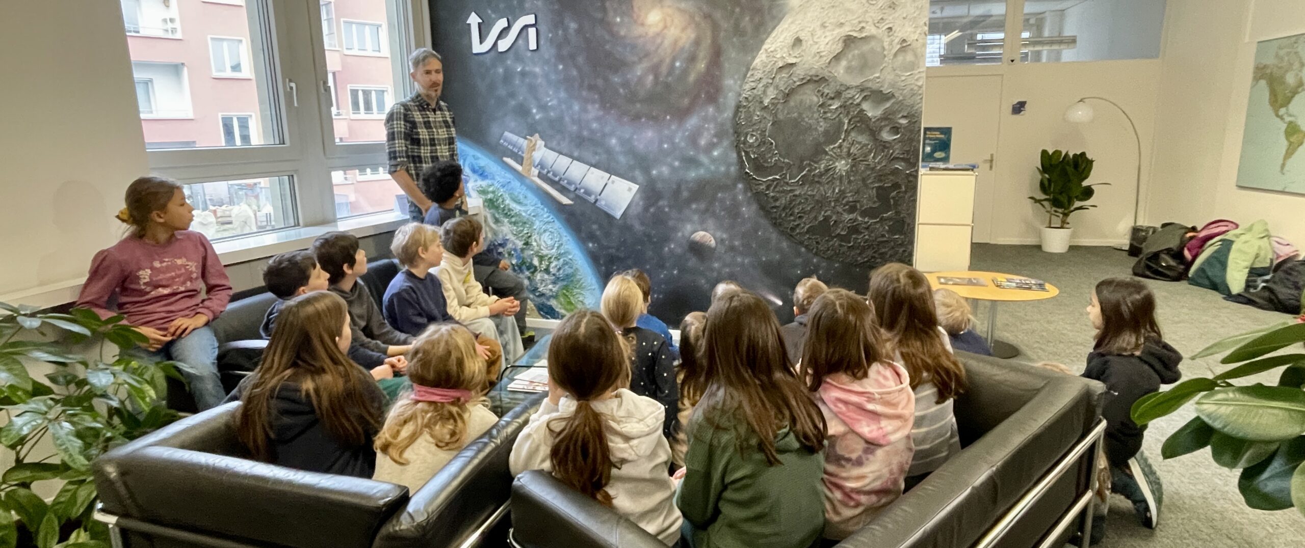 A school class visiting ISSI and looking at the ISSI Mural asking questions about space science.